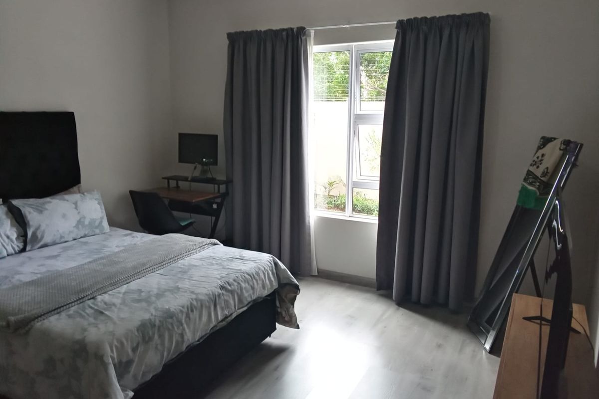 A well-lit bedroom featuring light-toned laminate flooring, neutral wall finishes, and a large window with curtain tracks.