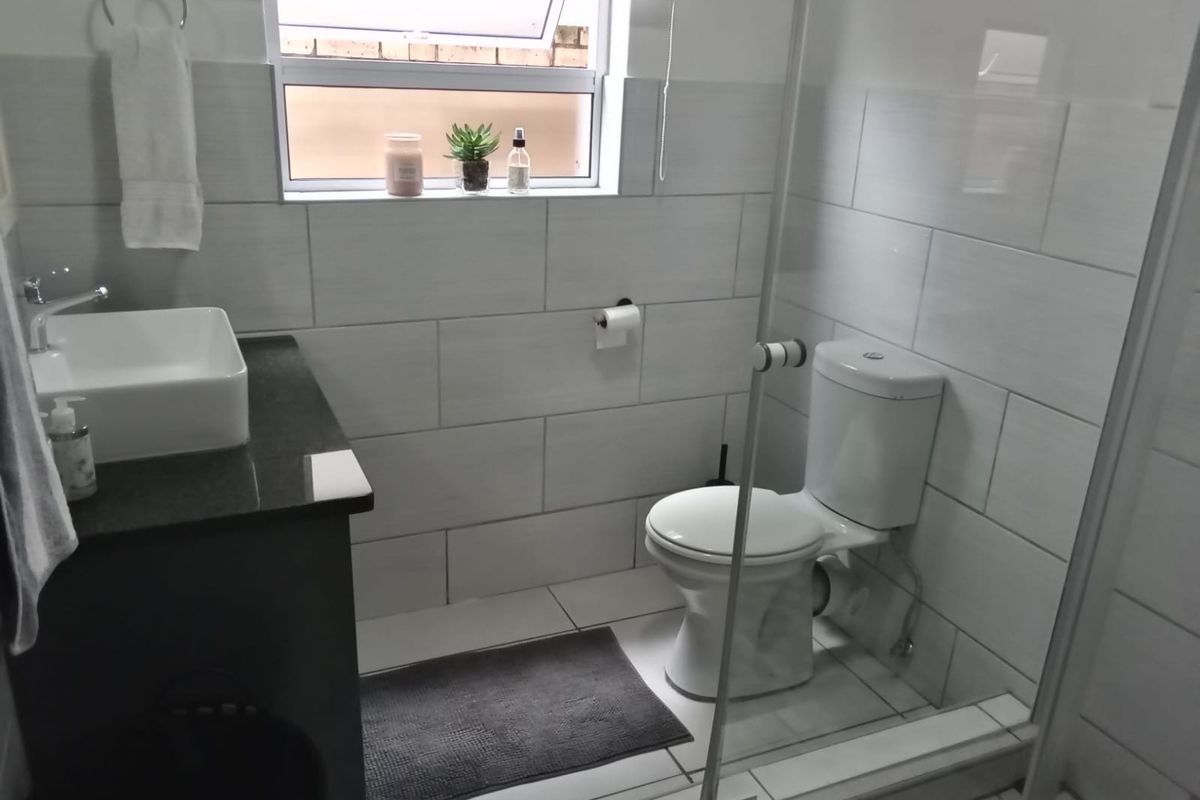 Modern bathroom featuring a vessel sink on a dark vanity, a white toilet, and a glass-enclosed shower with light-toned wall tiles.