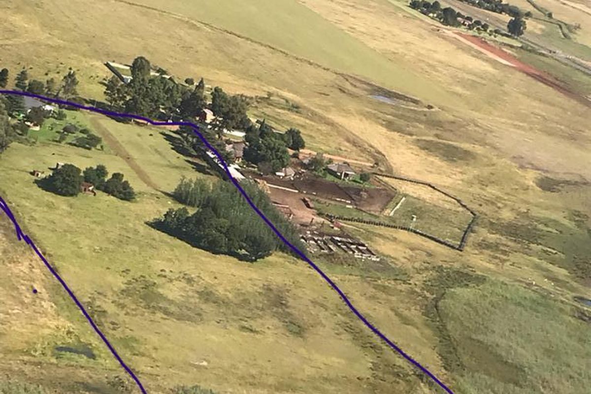 An aerial view of a large vacant residential land plot featuring open pasture, established trees, and perimeter fencing.