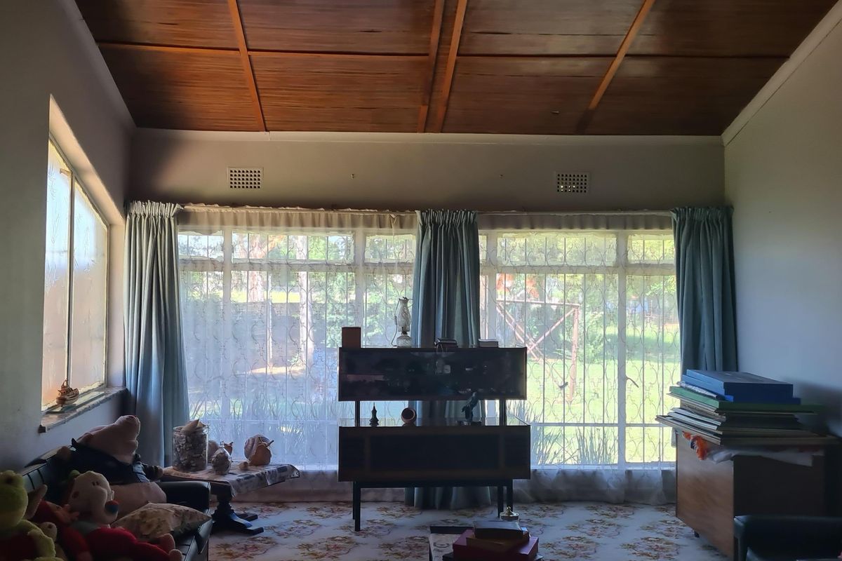 Spacious living room featuring a vaulted timber-paneled ceiling and large windows with security bars, offering potential for a modern update.