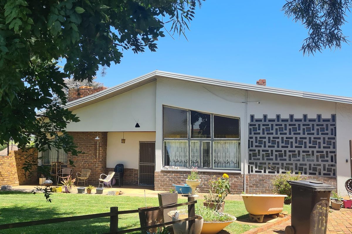 Rear view of a residential property featuring a paved patio, decorative brickwork, and an attached garage set within a landscaped garden.