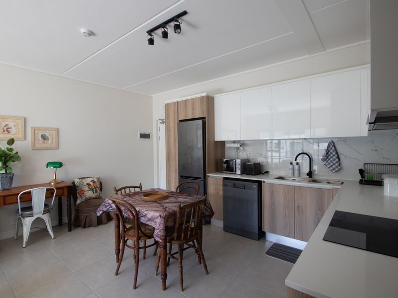 Modern open-plan kitchen featuring sleek white and wood-grain cabinetry, stone countertops, marble-look splashback, and integrated appliances, seamlessly flowing into a dining area.