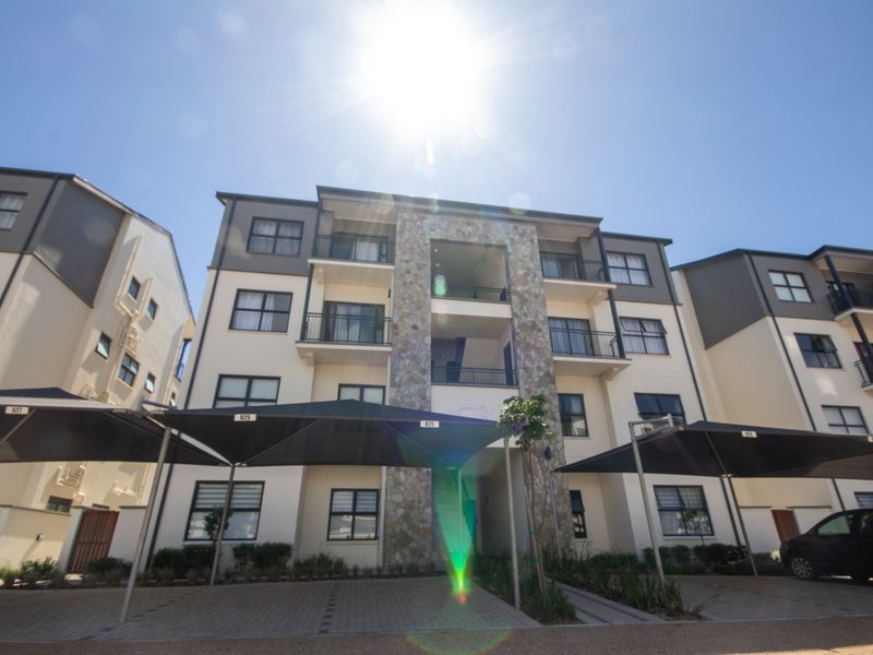 Front elevation of a multi-story apartment complex featuring stone cladding, private balconies, and covered parking bays.