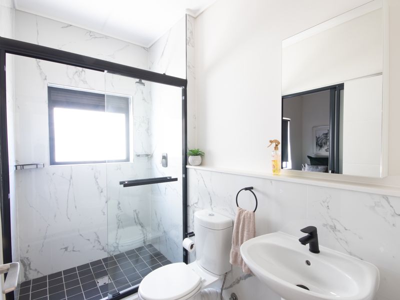 Modern bathroom featuring a walk-in shower with black-framed glass screen, marble-look wall tiling, pedestal basin with black tapware, and a wall-mounted mirror.