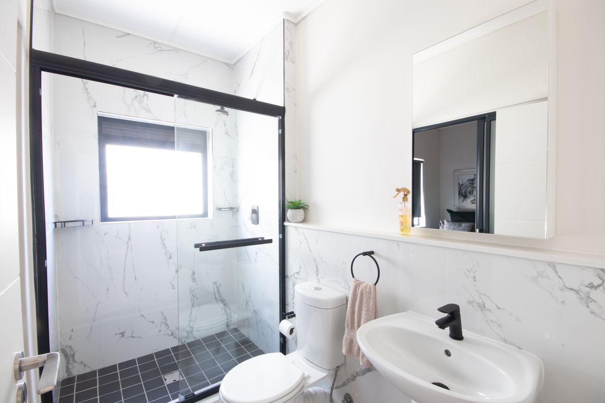 Modern bathroom featuring a walk-in shower with black-framed glass screen, marble-look wall tiling, pedestal basin with black tapware, and a wall-mounted mirror.