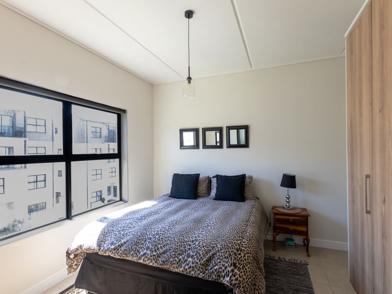 A well-lit bedroom featuring neutral walls, tiled flooring, and a large built-in wardrobe with wood-grain finish.