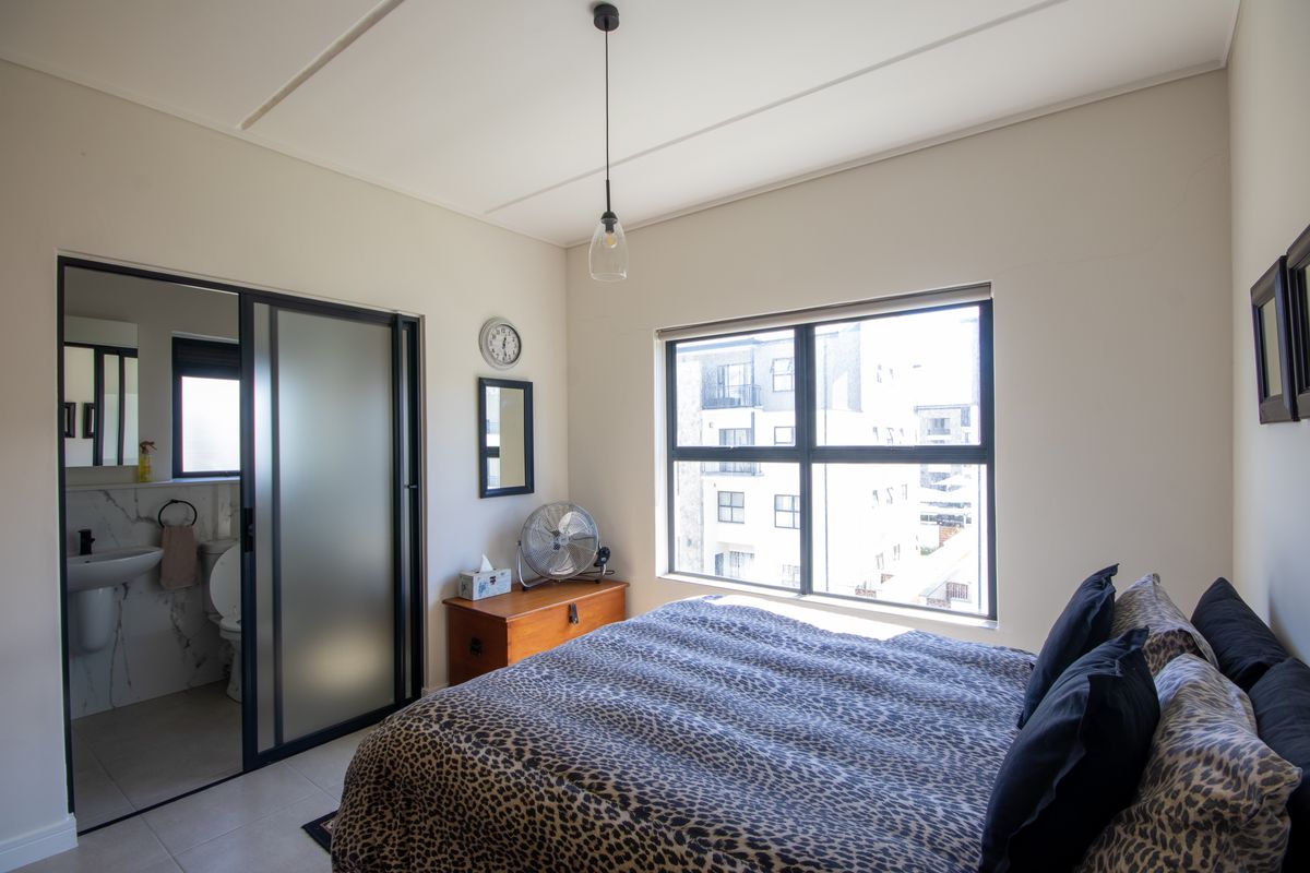 A well-lit bedroom featuring a modern en-suite bathroom with a sliding glass door, neutral finishes, and large windows providing natural light.