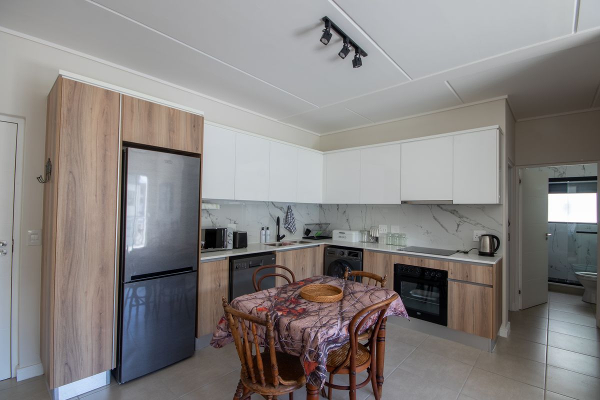 Modern kitchen featuring wood-grain and white cabinetry, marble-look splashback, integrated oven, electric hob, and track lighting, with an adjacent view into the bathroom.