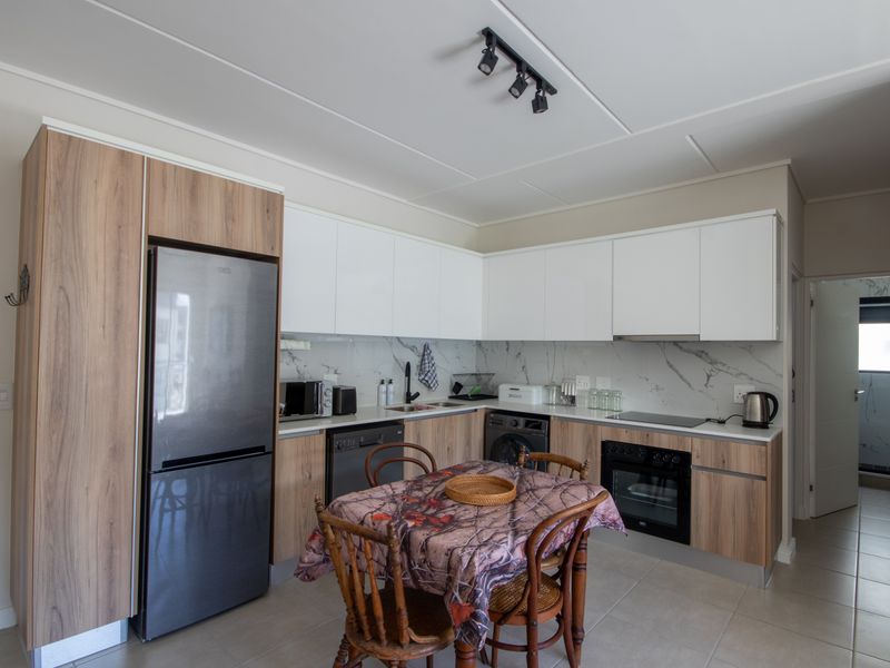 Modern kitchen featuring wood-grain and white cabinetry, marble-look splashback, integrated oven, electric hob, and track lighting, with an adjacent view into the bathroom.