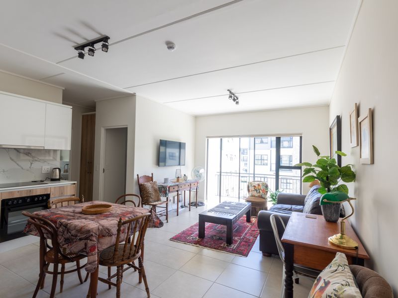 Modern open-plan living area featuring a contemporary kitchen with built-in appliances, tiled flooring, and direct access to a private balcony.