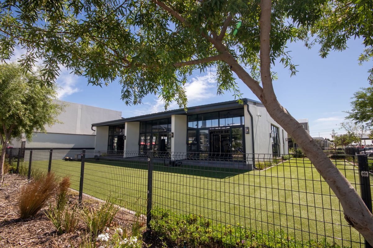 A well-maintained rear exterior view of the building featuring large glass windows, a modern metal roof, and a neat artificial lawn area.