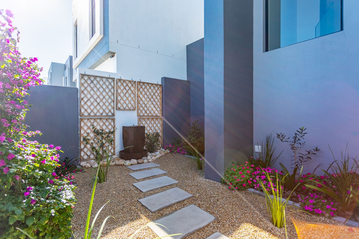 A landscaped rear garden area featuring a stone pathway, decorative gravel, a water feature, and modern architectural wall finishes.