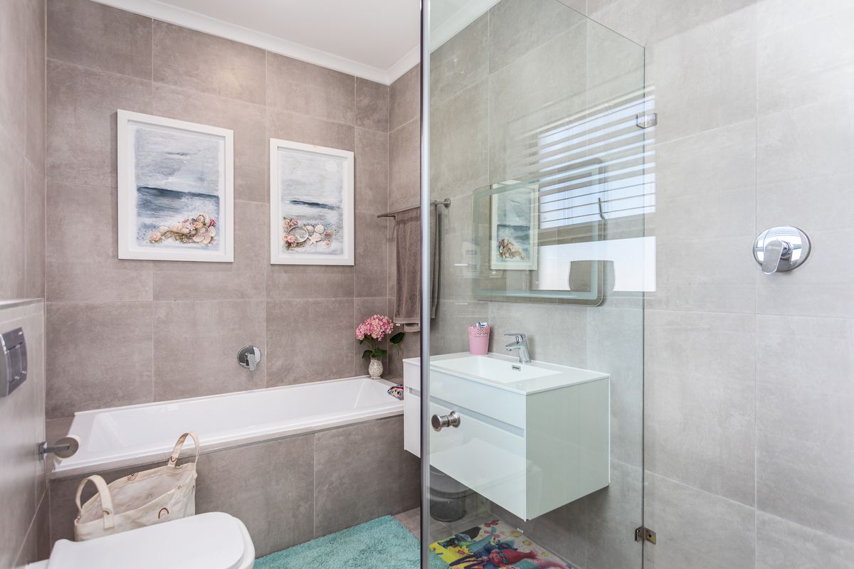 Modern bathroom featuring a built-in bathtub, wall-mounted vanity with basin, and a glass-enclosed shower with contemporary grey tiling.