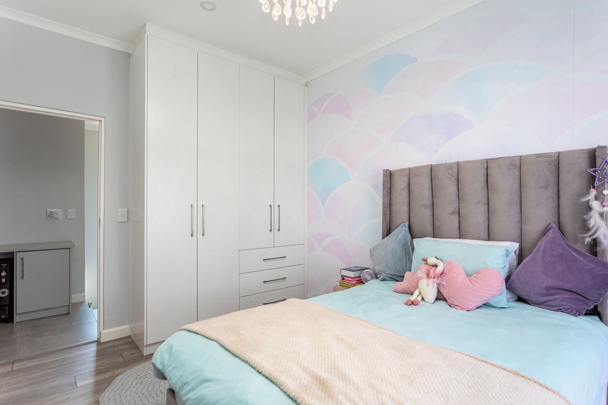 A well-maintained bedroom featuring built-in floor-to-ceiling wardrobes, laminate flooring, and a decorative feature wall.