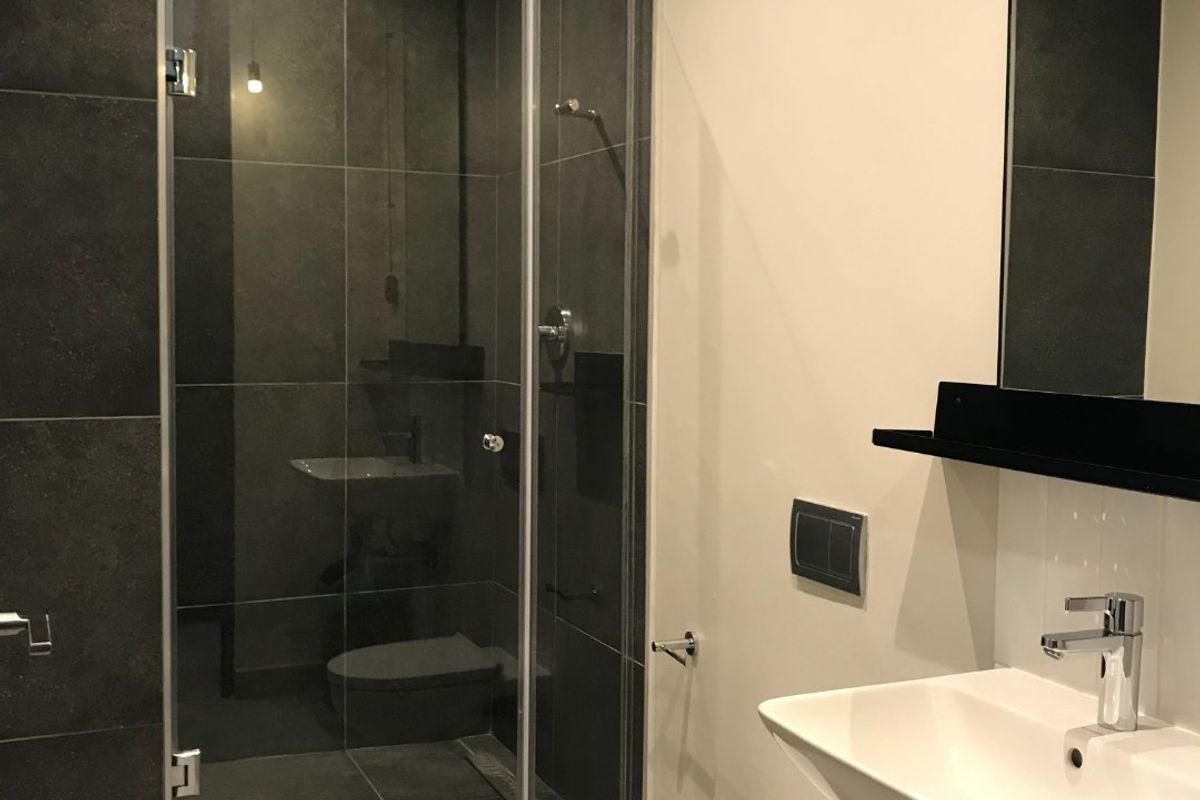 Modern bathroom featuring a glass-enclosed walk-in shower, wall-mounted toilet, and a sleek basin with chrome fixtures, finished with dark charcoal wall tiles.