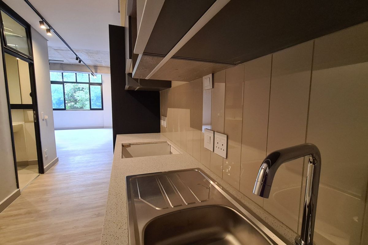 Modern kitchen area featuring stone countertops, stainless steel sink, tiled backsplash, and sleek cabinetry, leading into an open-plan living space.