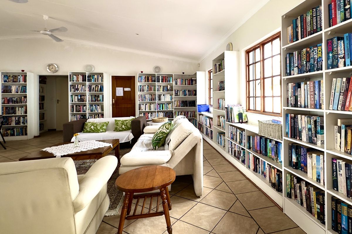 Spacious living area featuring extensive built-in floor-to-ceiling bookshelves, tiled flooring, and large windows providing ample natural light.