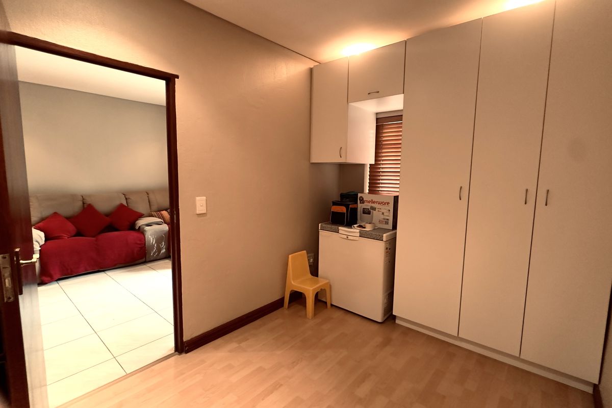 A bedroom featuring built-in cupboards, laminate flooring, and wooden blinds, with an open doorway leading to an adjacent living area.