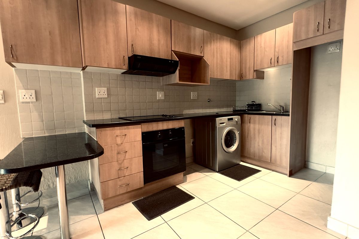 Compact kitchen featuring laminate cabinetry, granite countertops, built-in oven, electric hob, extractor fan, and tiled flooring with integrated laundry space.