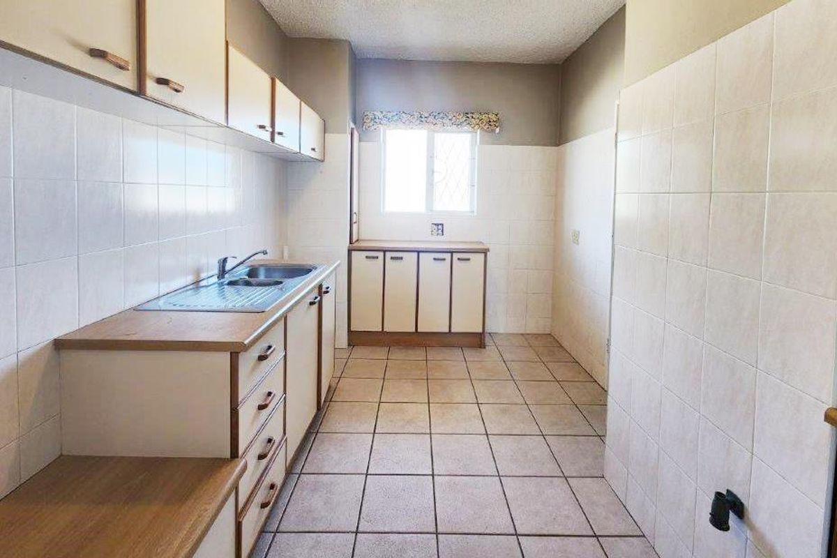 A functional, dated kitchen featuring tiled walls, ceramic floor tiles, and laminate cabinetry with a stainless steel sink.