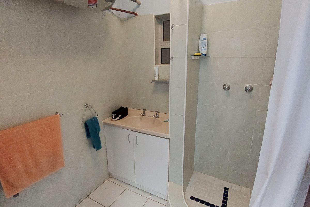 A functional bathroom featuring a shower enclosure, vanity basin, and exposed water heater unit with associated plumbing.