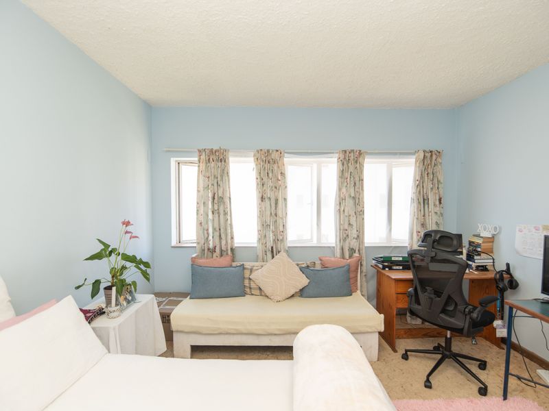 A bedroom featuring light blue walls, a textured ceiling, and large casement windows allowing natural light into the space.