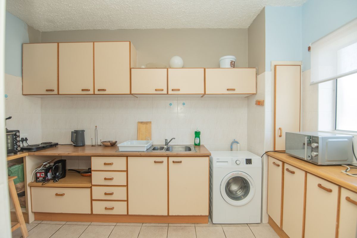 A functional kitchen featuring laminate cabinetry, tiled backsplash, and integrated laundry plumbing, offering a dated aesthetic ready for modernization.