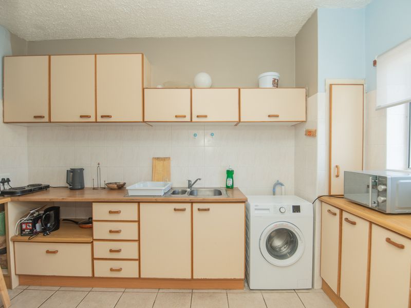 A functional kitchen featuring laminate cabinetry, tiled backsplash, and integrated laundry plumbing, offering a dated aesthetic ready for modernization.