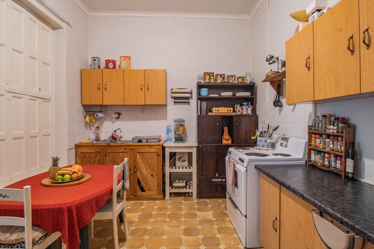 A dated kitchen featuring wooden cabinetry, a freestanding stove, and vinyl flooring, offering a functional layout with potential for modernization.