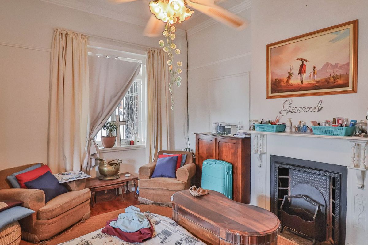 A cozy living room featuring a traditional fireplace with a decorative mantelpiece, high ceilings, and a ceiling fan.