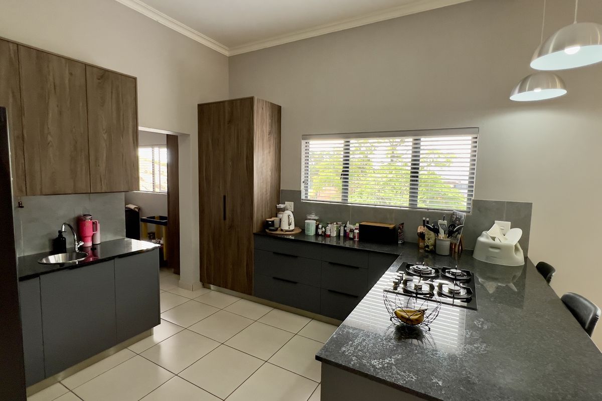 Modern kitchen featuring dark grey cabinetry, wood-grain upper cabinets, stone countertops, a built-in gas hob, and a breakfast bar island.
