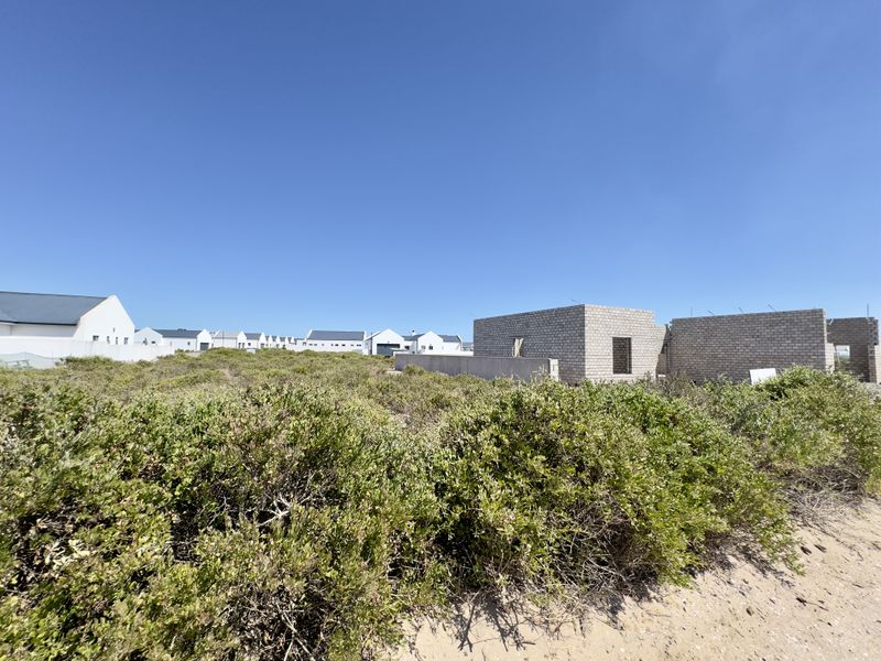 A vacant residential plot featuring partially constructed masonry walls and native coastal vegetation in a developing neighborhood.