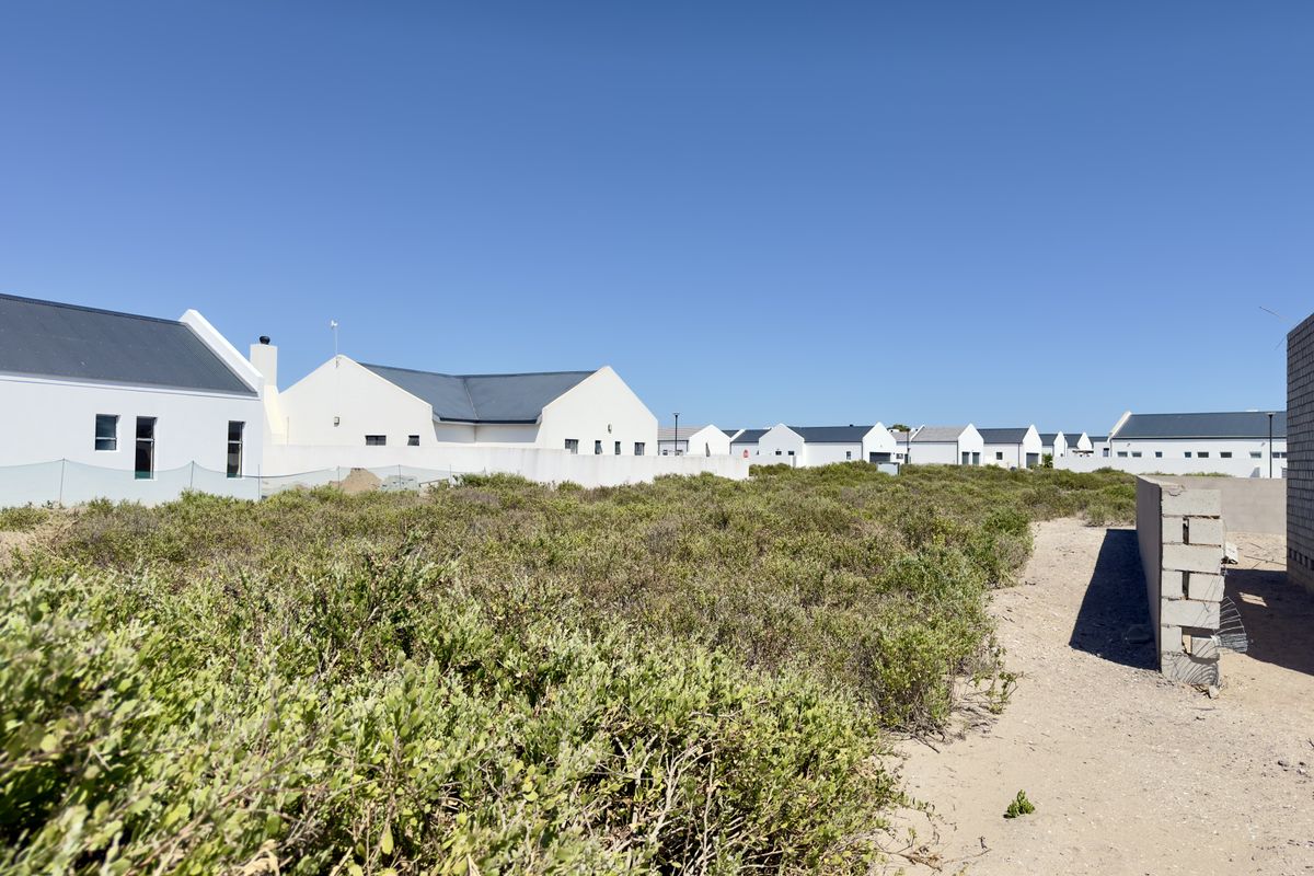 A view of a vacant residential plot featuring natural vegetation, adjacent to established housing developments in a coastal or estate setting.