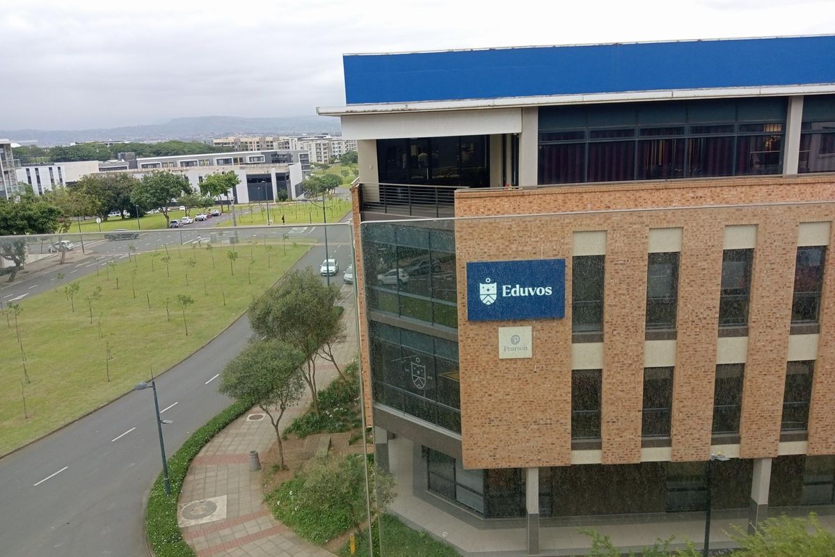 An elevated view of a modern brick-faced commercial building featuring glass curtain walls and prominent signage, situated near a landscaped road.