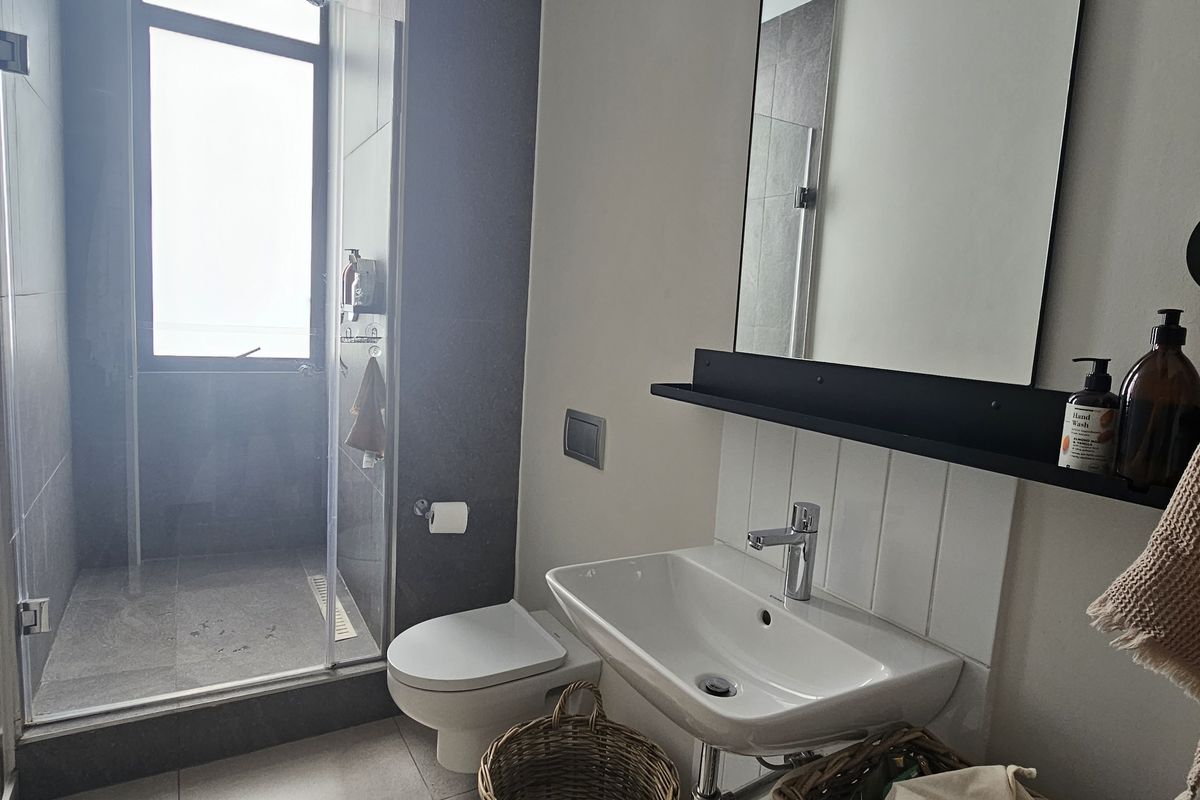 Modern bathroom featuring a glass-enclosed shower, wall-mounted toilet, and a sleek vanity basin with a contemporary mirror and shelf.