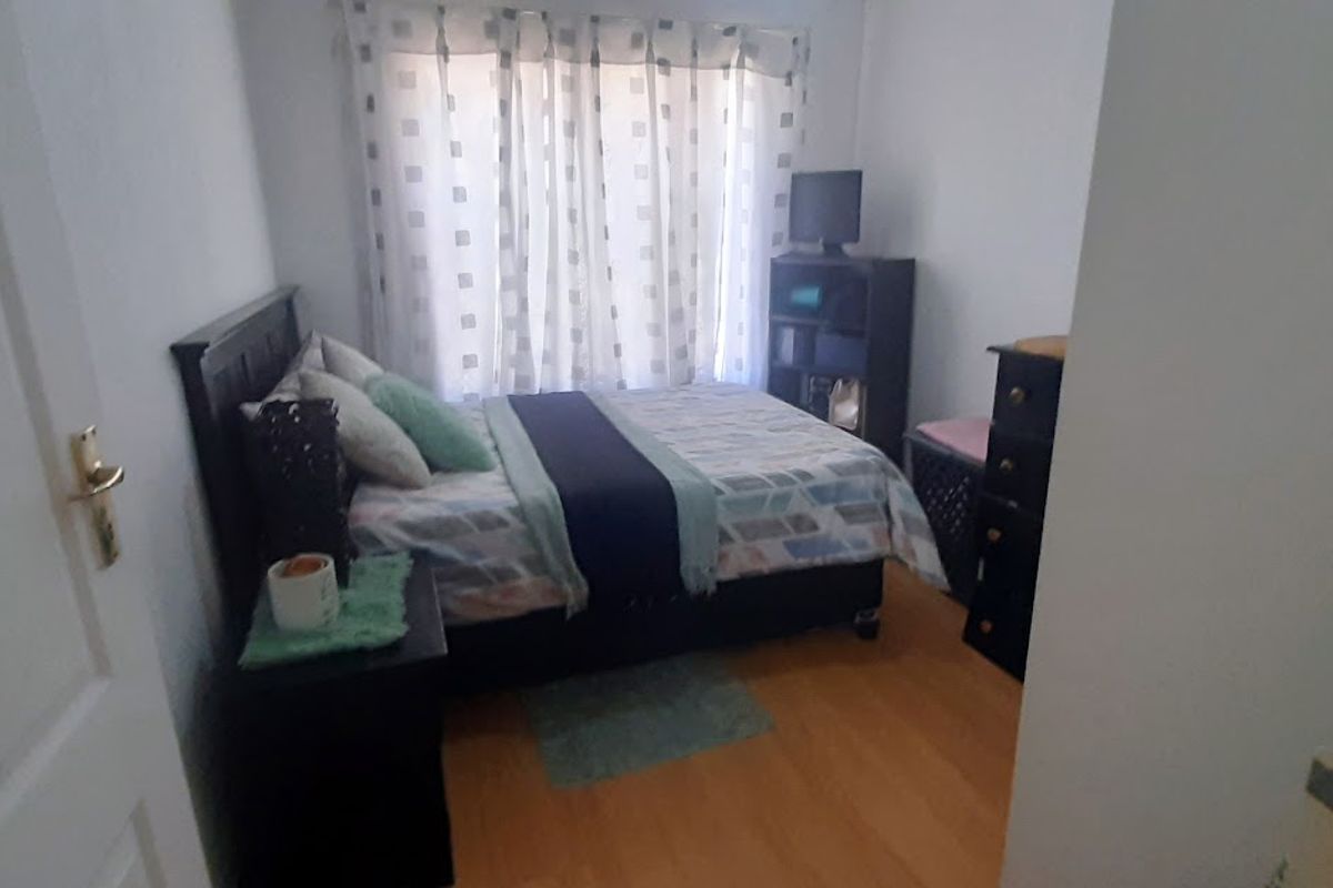 A standard bedroom featuring laminate flooring and large windows with curtains, providing a functional and comfortable sleeping space.