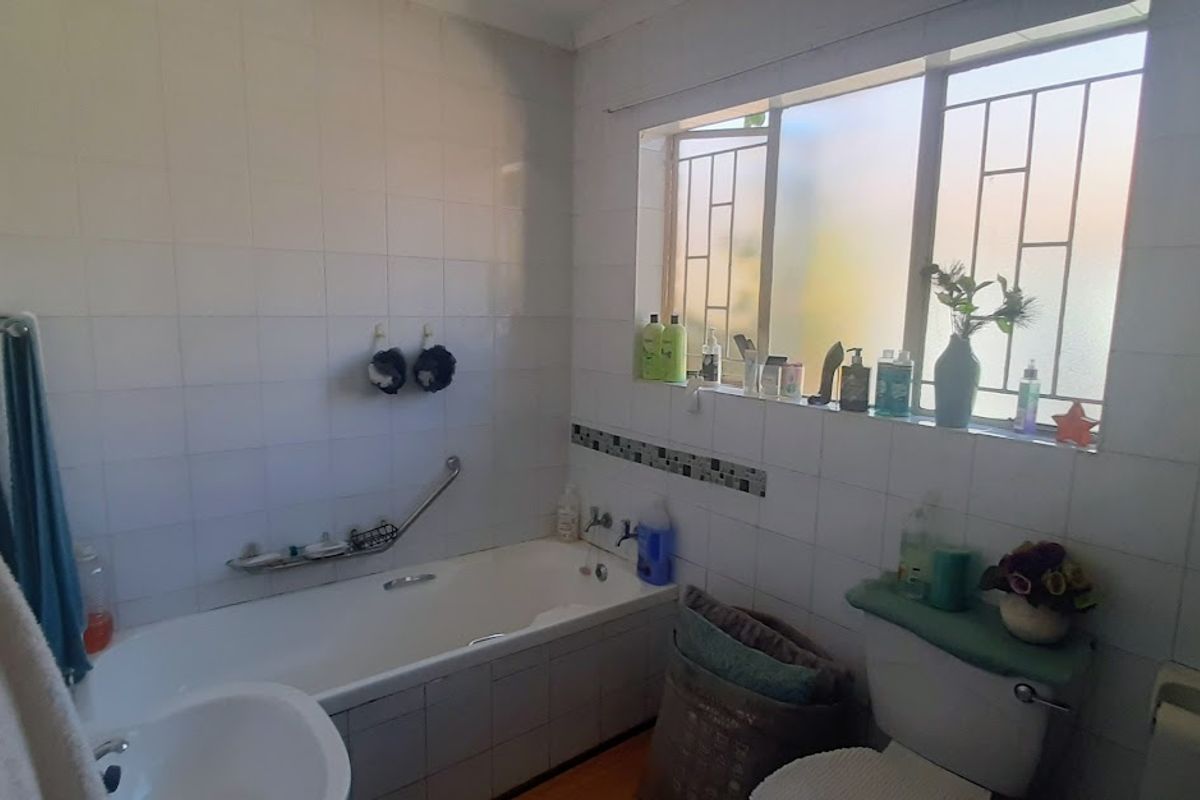 A functional bathroom featuring a bathtub, toilet, and tiled walls with security bars on the window.