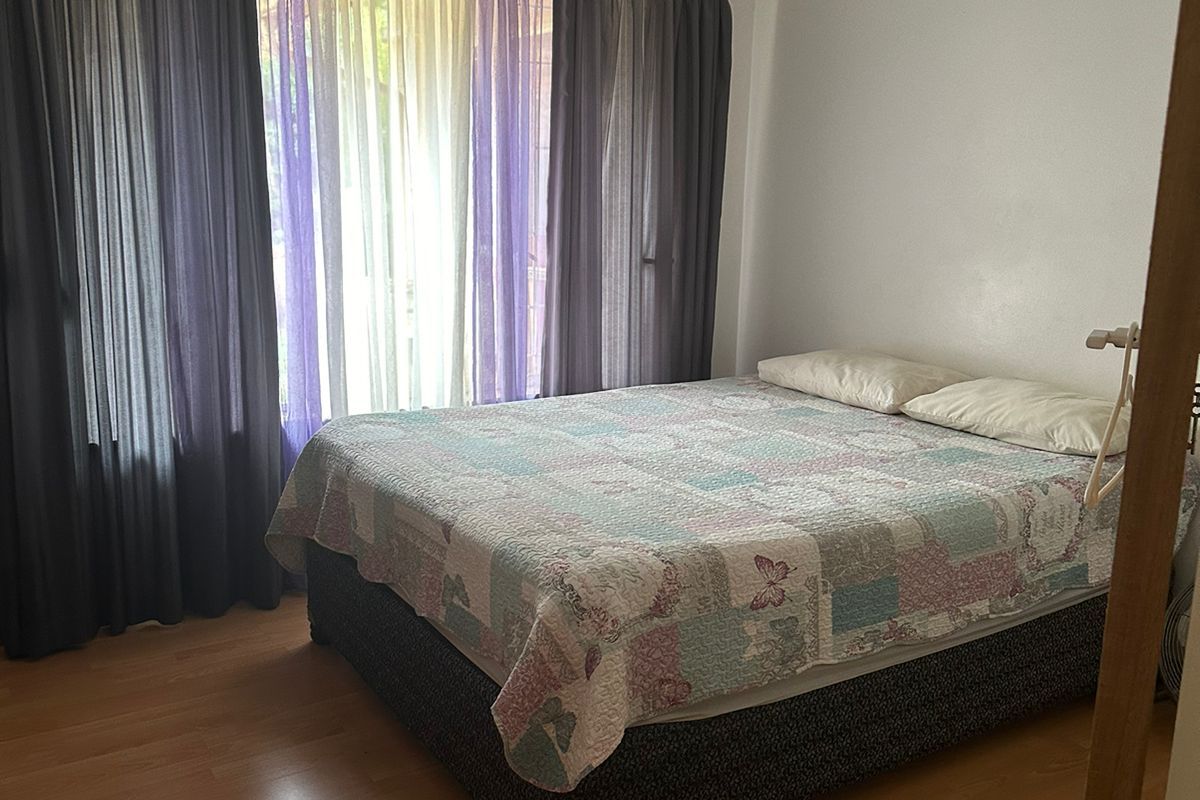 A bedroom featuring laminate flooring and large windows dressed with layered curtains, providing a simple and functional living space.