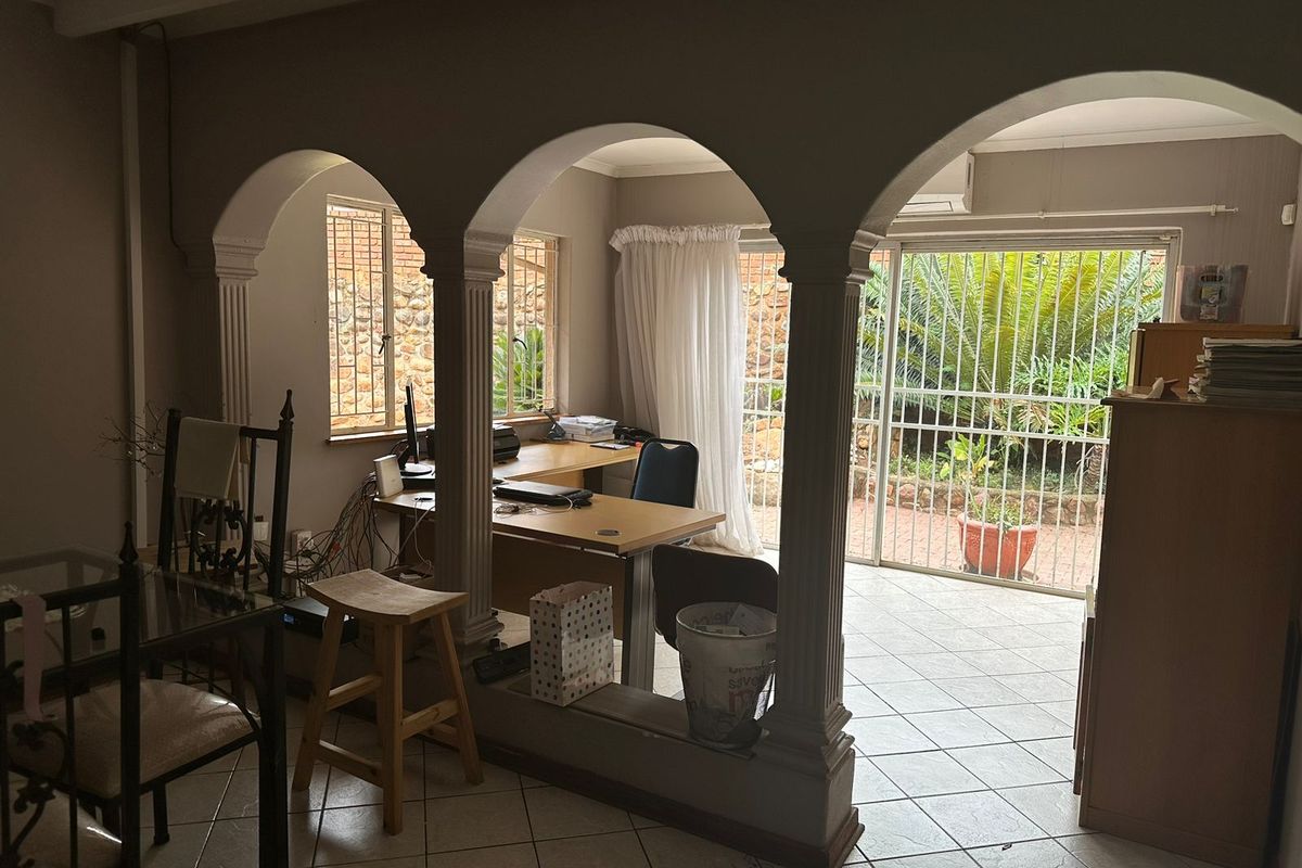 A multi-purpose living area featuring decorative archways, tiled flooring, and direct access to an outdoor patio through security gates.