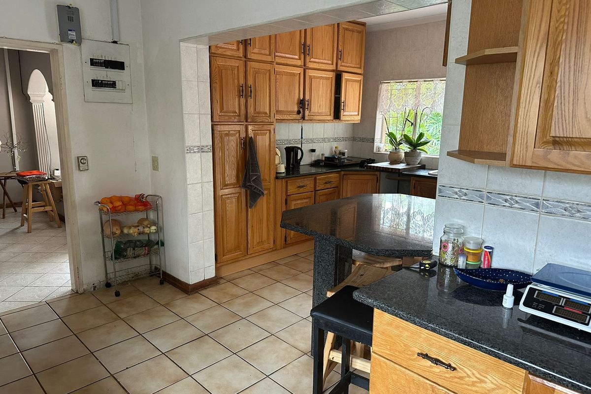 A functional kitchen featuring traditional oak cabinetry, granite countertops, and a breakfast bar, with tiled flooring and direct access to adjacent living areas.