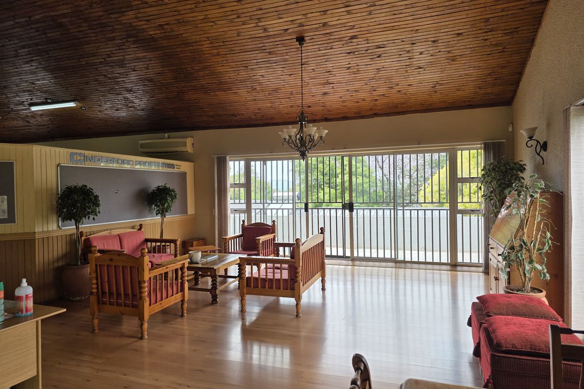 Spacious living area featuring a high vaulted timber ceiling, laminate flooring, and large sliding glass doors with security bars leading to the exterior.