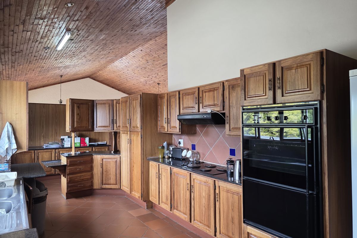 Spacious kitchen featuring extensive timber cabinetry, built-in double oven, extractor fan, and tiled flooring under a high vaulted timber-clad ceiling.
