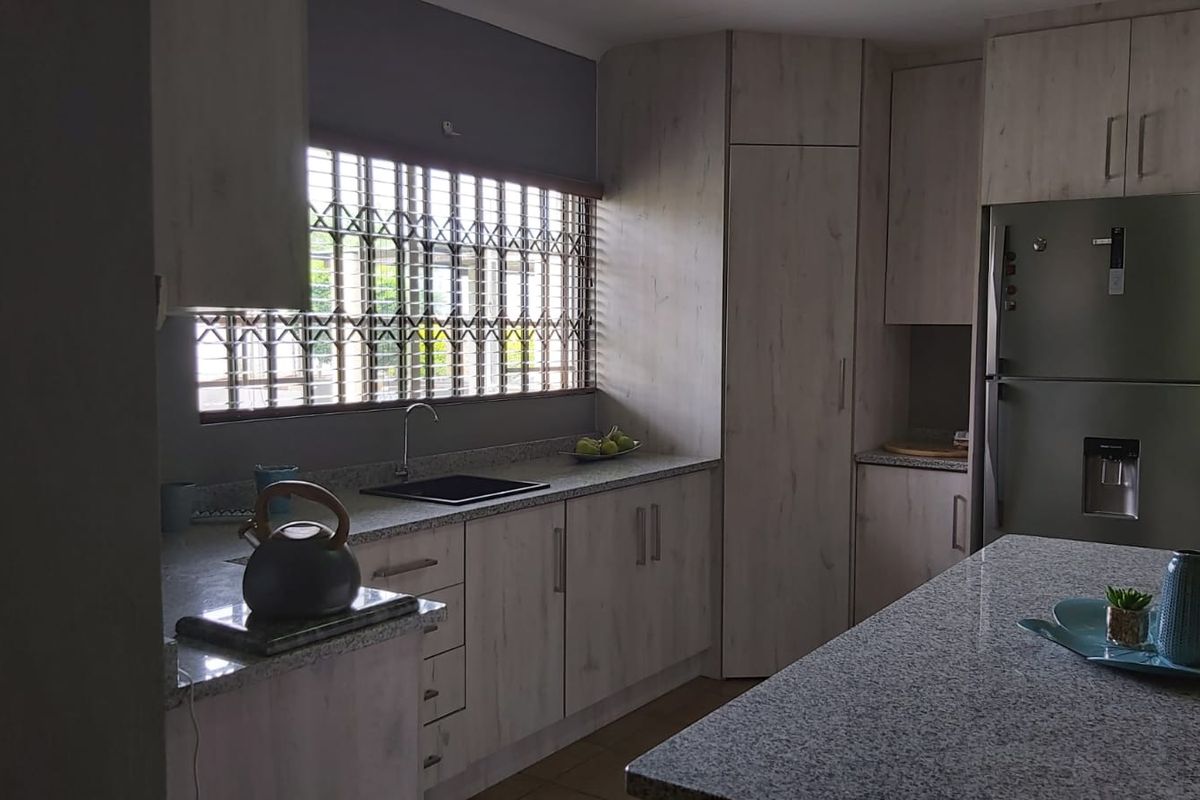 Modern kitchen featuring light wood-grain cabinetry, granite countertops, a central island, and a built-in sink with security bars on the window.