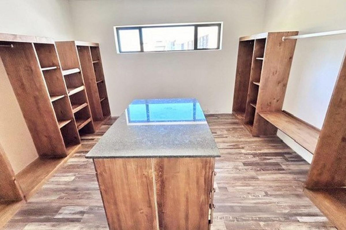 A spacious walk-in closet featuring custom built-in wooden cabinetry, a central island with a stone countertop, and wood-look flooring.