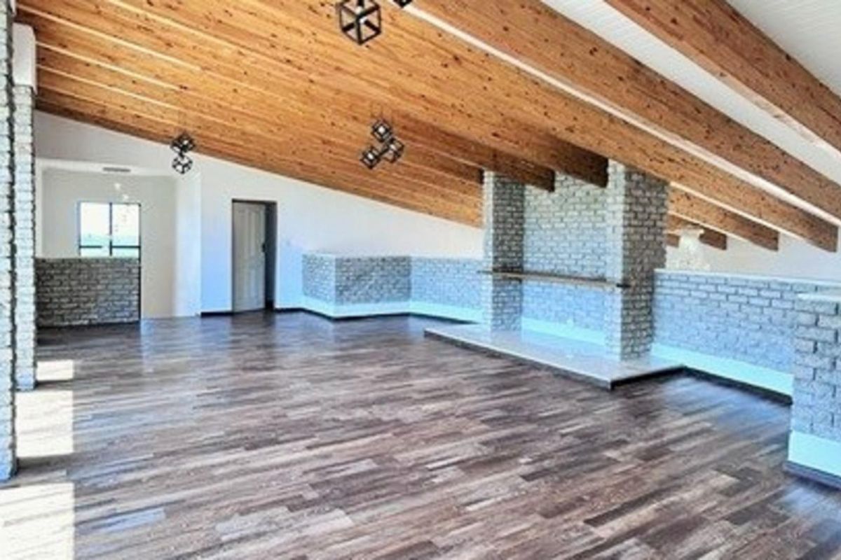 Spacious living area featuring vaulted timber-beamed ceilings, exposed brick feature walls, and durable wood-look flooring in an open-plan layout.
