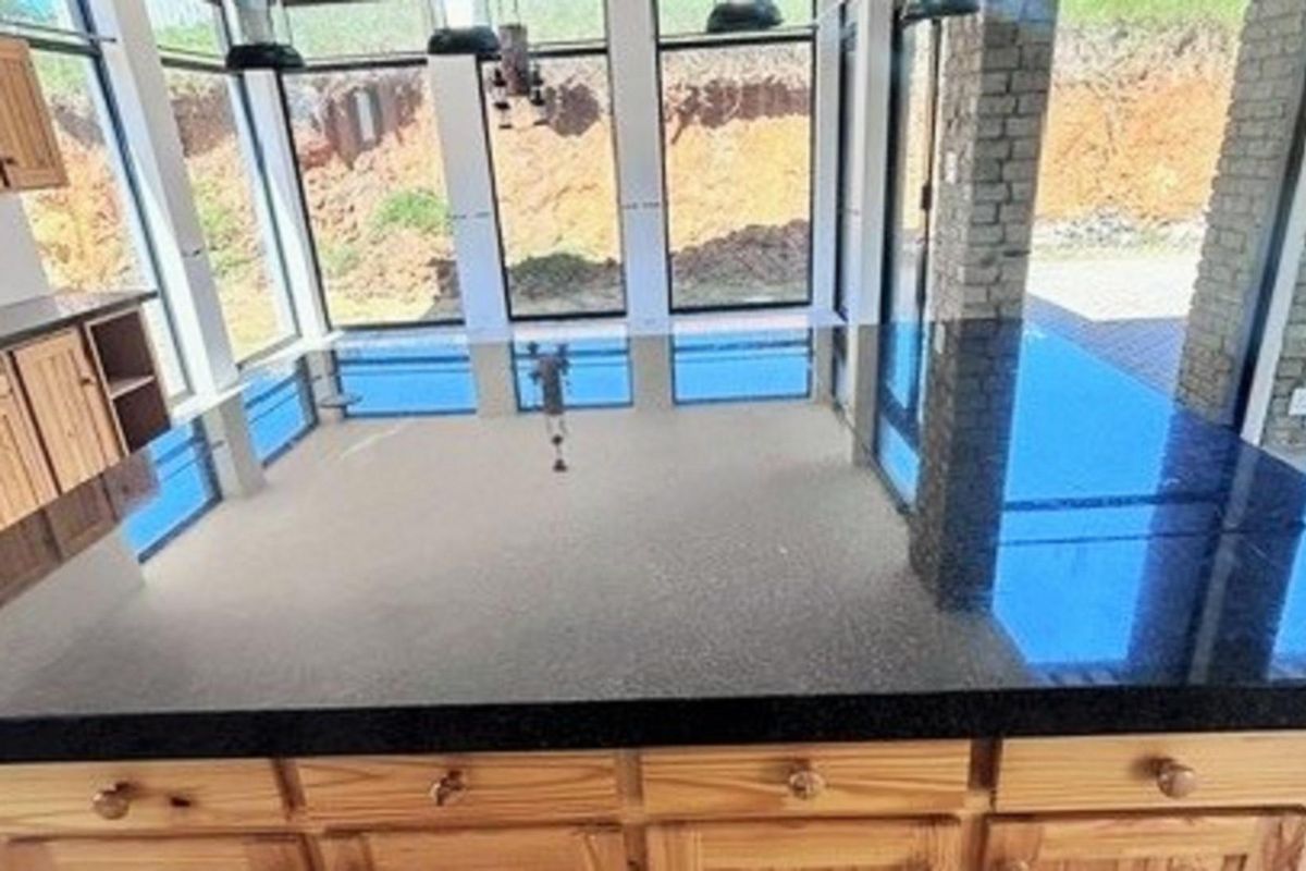 A modern kitchen featuring a large black granite island countertop, natural wood cabinetry, and expansive floor-to-ceiling windows overlooking the rear exterior.