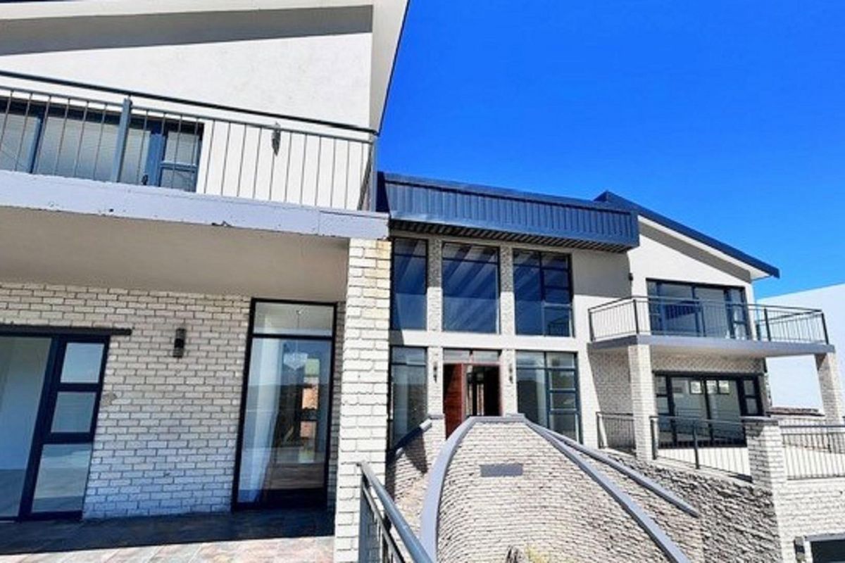 A modern multi-level residential exterior featuring white brickwork, large glass windows, metal railings, and a spacious balcony area.