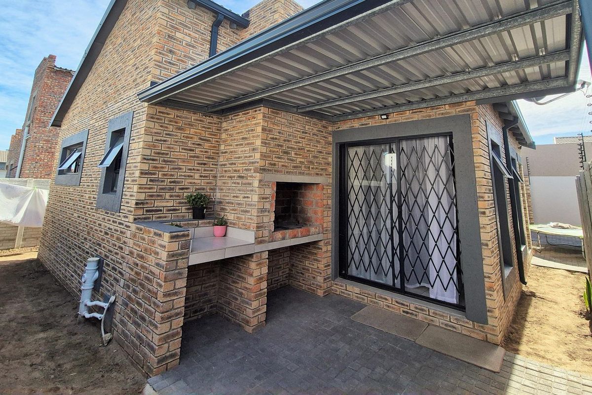 Covered outdoor patio area featuring a built-in brick braai and prep counter, adjacent to the main house structure with paved flooring.