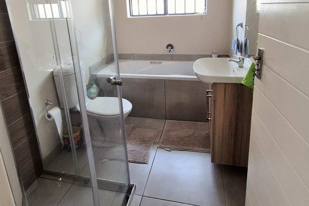 A functional bathroom featuring a glass-enclosed shower, a built-in bathtub, a vanity basin with storage, and tiled flooring.
