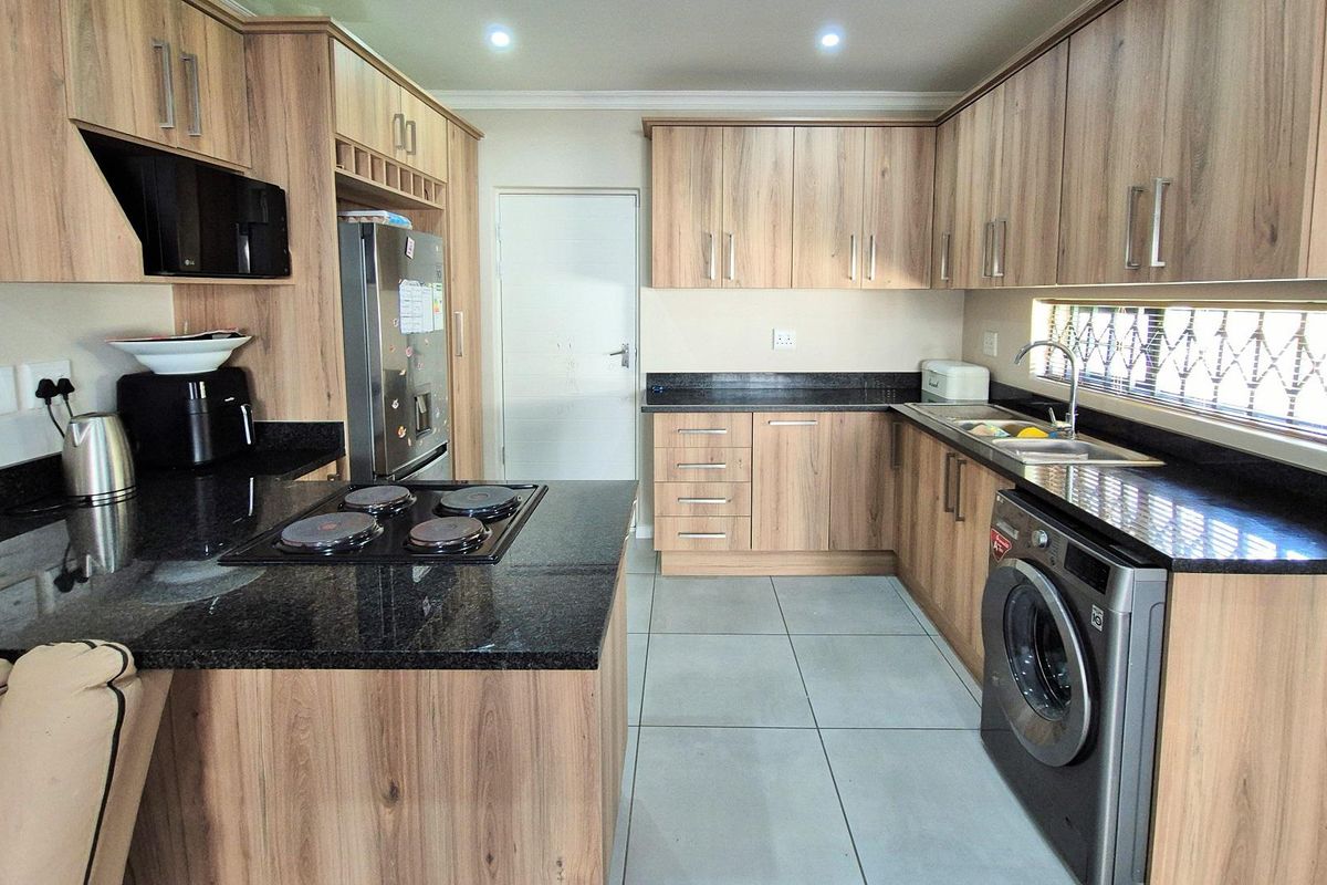Modern kitchen featuring wood-grain cabinetry, dark granite countertops, integrated electric hob, built-in oven, and tiled flooring.